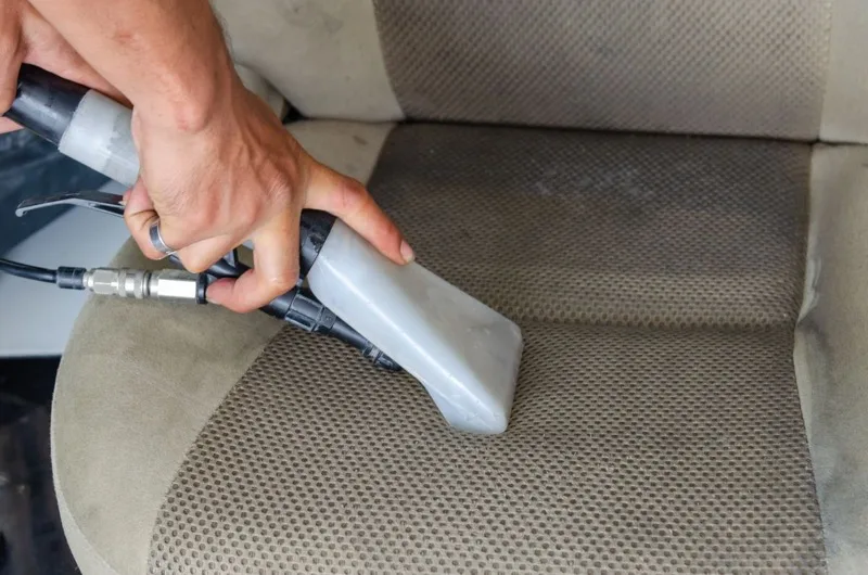 Detailer deep-cleaning a car seat with a steam cleaner
